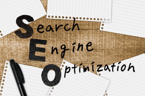 「SEO」の文字と「Search Engine Optimization」のメモ、そして万年筆が置かれた木目調のデスク。検索エンジン最適化をイメージしたビジネスフォト